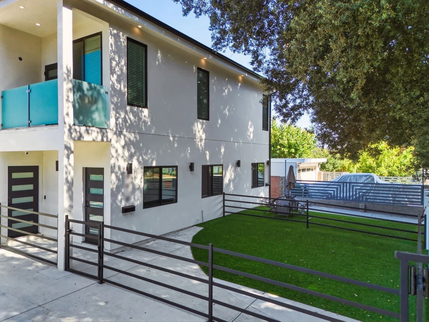 Completed two-story ADU at the Kentland project by Yeganeh Inc., seen from the side yard with a glass balcony, black-framed windows and a fenced lawn