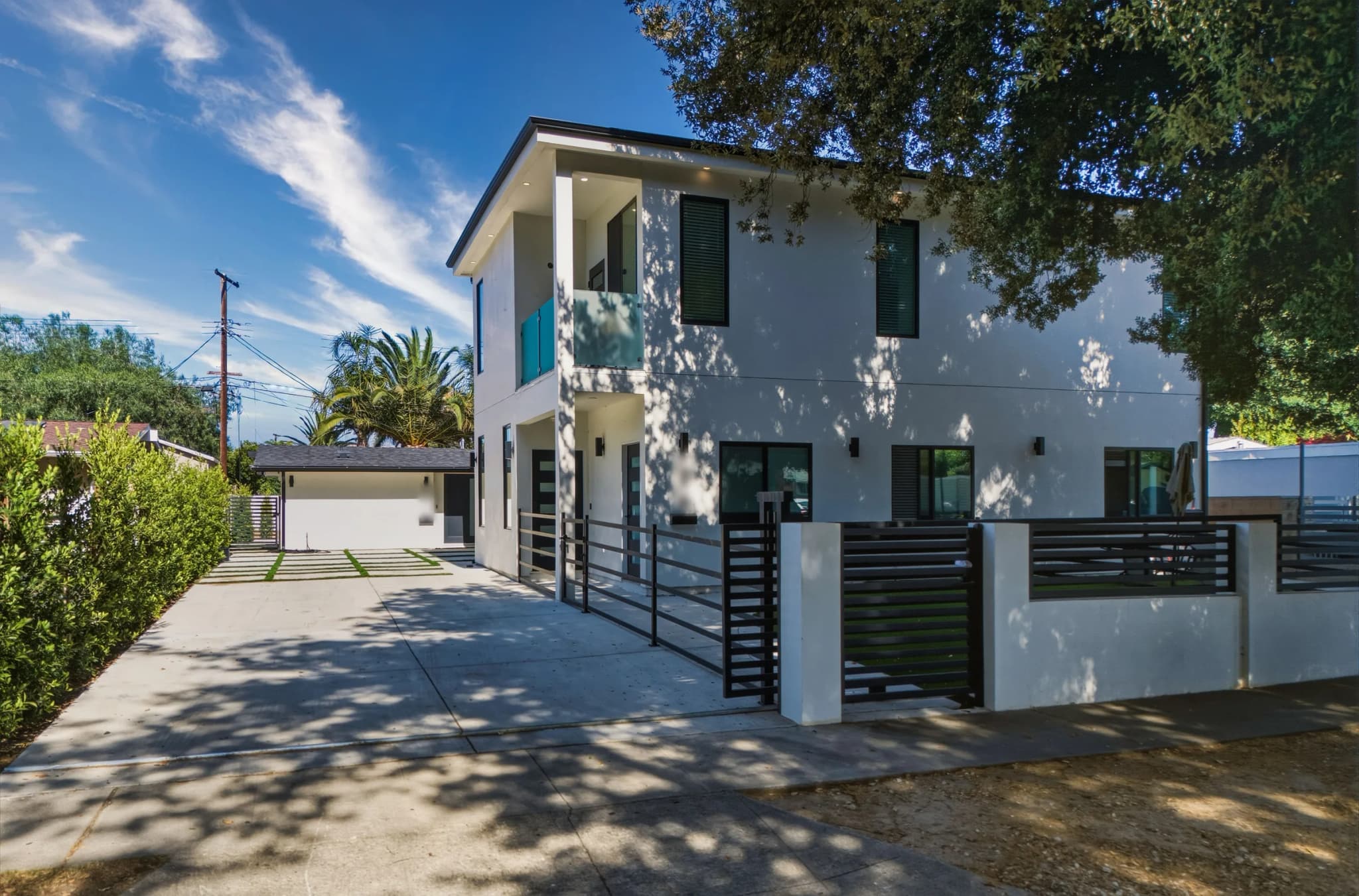 Completed two-story ADU at the Kentland project by Yeganeh Inc., a white modern building with a glass balcony, seen from the driveway beside a horizontal metal gate